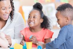 Teacher playing and smiling with two of her preschoolers.