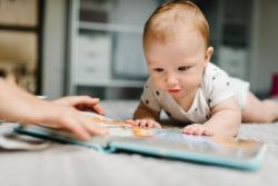 A baby on the floor with a book.