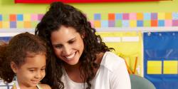 Teacher and young girl sitting at a desk in a classroom.