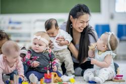 Teacher in a classroom with babies sitting on the floor with blocks