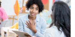 Female teacher in a classroom speaking to another female teacher