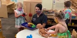 Teacher in a classroom with three young children, all wearing masks.