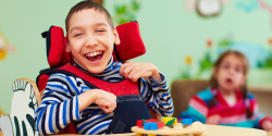 a happy child sitting in a wheelchair and a child with specialized glasses in the background