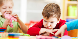 An unhappy child sitting at a table with others.