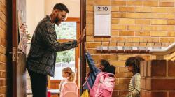 A male teacher high fiving a student on the way into the classroom