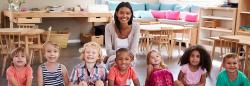 Group photo of teacher smiling with preschool students in classroom