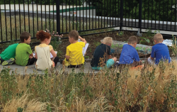 Row of children sitting outside near a garden