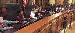 A group of preschool children sits at a city hall desk.