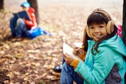 A young girl draws and takes notes in a forest