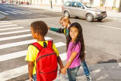 Three children of different races and ethnicities walk to school together.