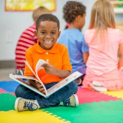 A young boy smiling and reading a book