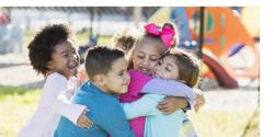 A group of diverse young children hugging on a playground