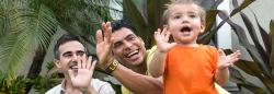 Two male parents play outdoors with their child.