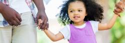 Young girl holding parent's hands outside