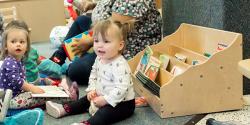 Young children sitting next to a bookshelf.