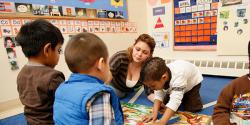 A teacher observing young children who are exploring a map in a classroom.