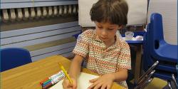 A young child at a desk writing on a piece of paper. 