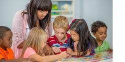 A teacher showing children a picture on a table.