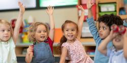 Children raise their hands to engage in a circle time discussion. 