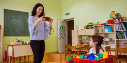 A teacher using a device to document a child playing in the classroom.