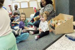 Toddlers playing in a classroom on the floor, sitting with three teachers