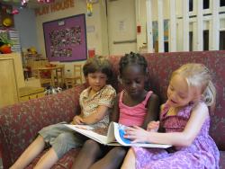 three preschoolers in a classroom sitting on a chair reading a book