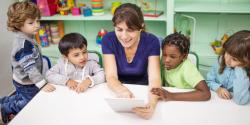 children looking at a tablet with a teacher