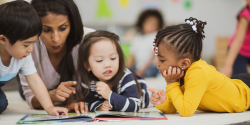 A teacher guides children reading a book.