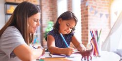 A teacher overseeing a child drawing to illustrate a story.