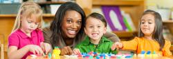 Preschool teacher helping three students build with blocks