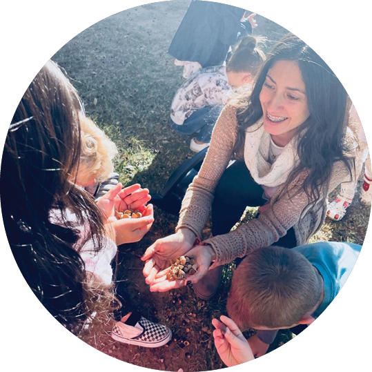 A teacher showing children acorns outside.