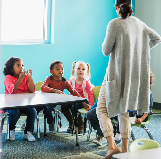 teacher standing in front of a table of students who are all looking at her