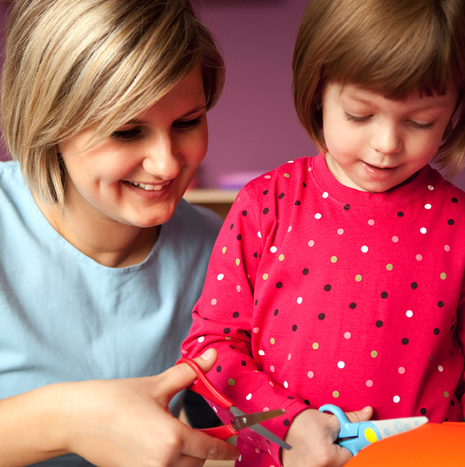 teacher helping a student cut a piece of paper with scissors