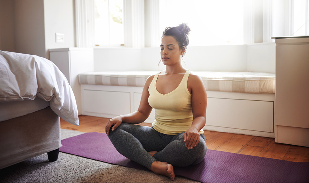 woman doing yoga sitting cross-legged on the floor of a bedroom